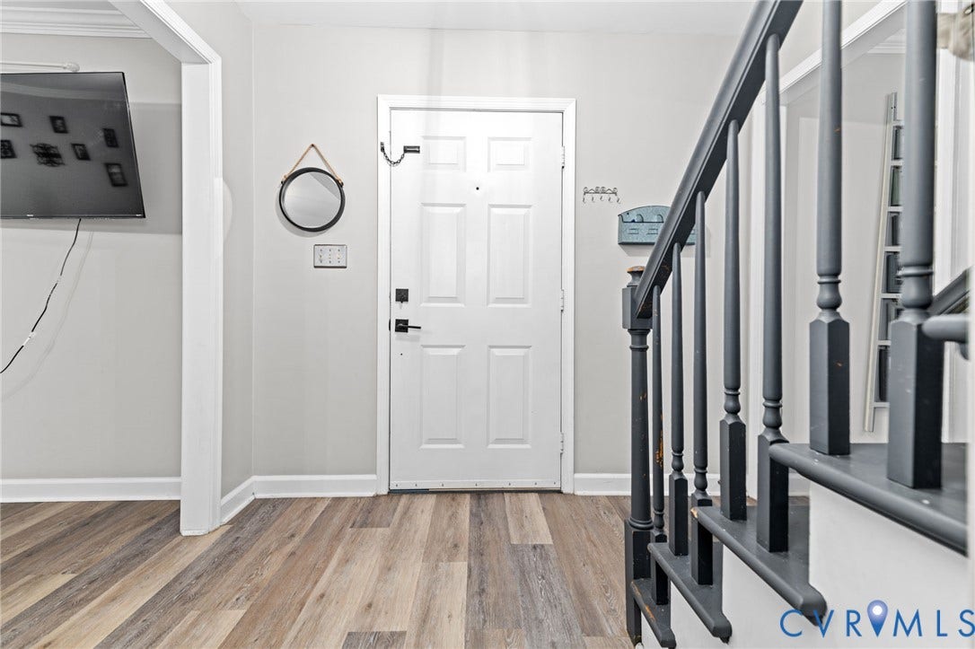 Entryway featuring wood-finish flooring, a white paneled door, and a staircase with dark balusters