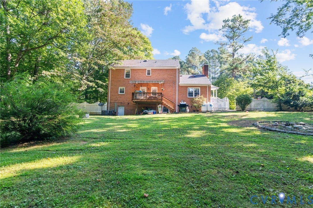 Brick exterior with a multi-level deck, white picket fencing, and mature trees