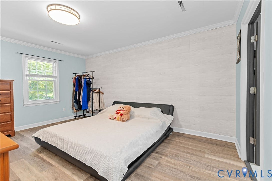 Wood-finish flooring, white wood panel accent wall, window with white trim, and crown molding