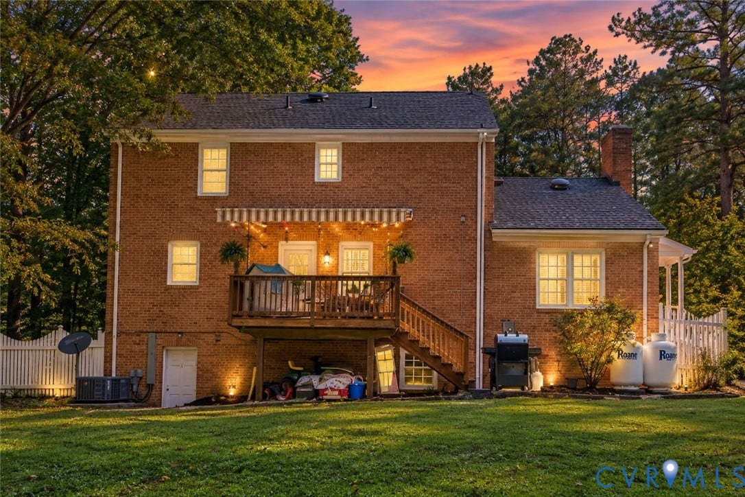 Brick exterior with a multi-level deck, white picket fence, and mature trees