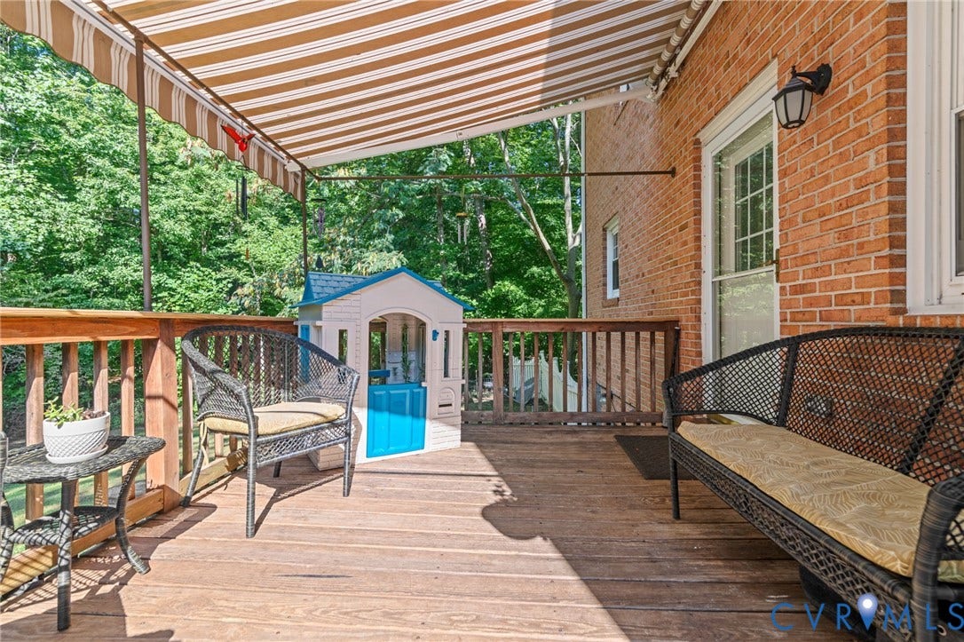 Expansive wood deck with a retractable awning, brick exterior, and outdoor lighting fixture