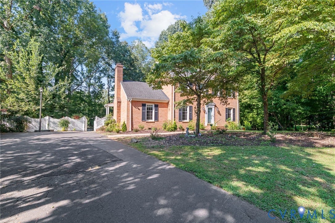 Traditional brick exterior with black shutters, mature tree landscaping, and a white picket fence