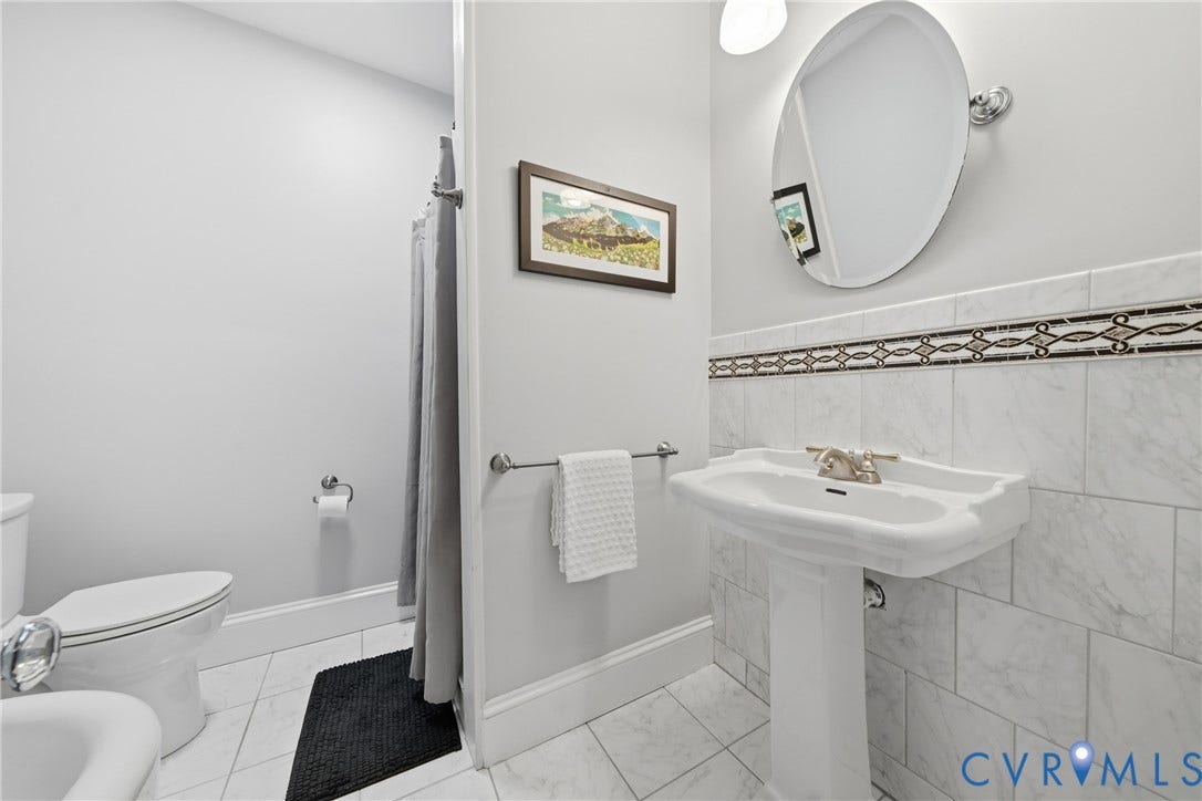 1500 Avondale Avenue, Bellevue, Richmond, VA 23227 Pedestal sink with a polished brass-tone faucet, white tiled walls with a mosaic accent, and a coordinating oval mirror