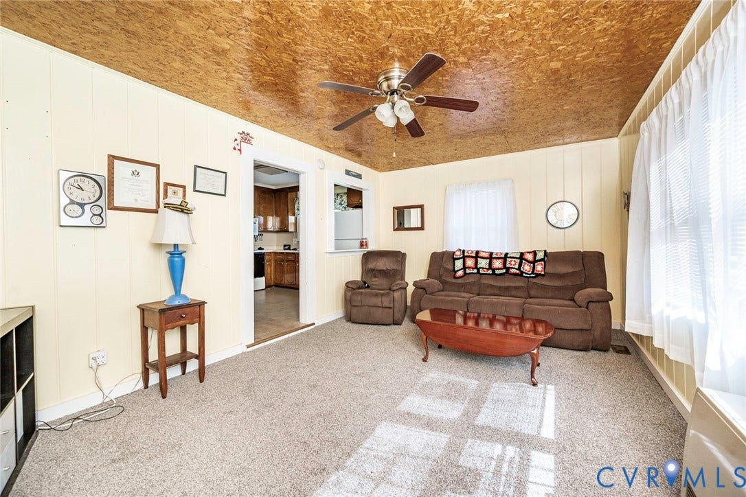 4912 Water View Road, Water View, Jamaica, VA 23180 Carpeted living area featuring a ceiling fan with light kit, paneling walls, and an open doorway leading to a kitchen