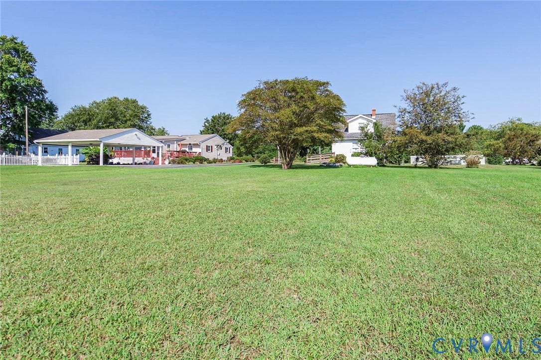 4912 Water View Road, Water View, Jamaica, VA 23180 Expansive lawn with mature trees, white picket fencing, and a covered carport structure