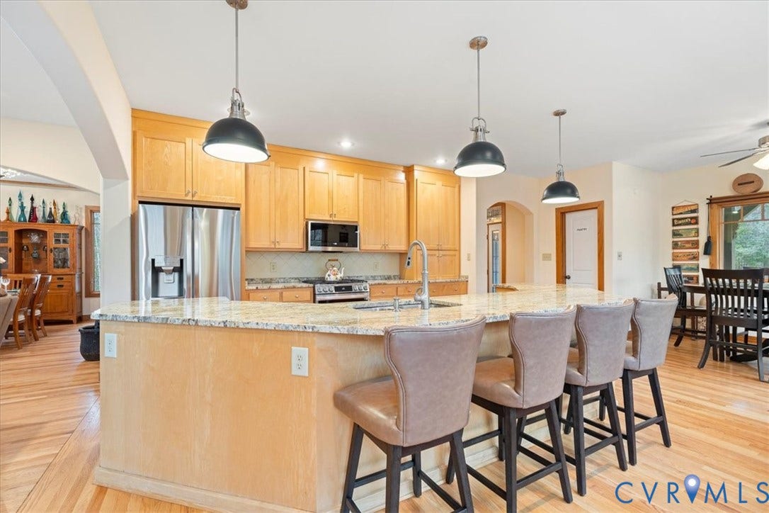 8908 Thomas Higgs Court, Toano, VA 23168 Open-concept kitchen featuring an island with seating, stainless steel appliances, light wood cabinetry, and wood-finish flooring