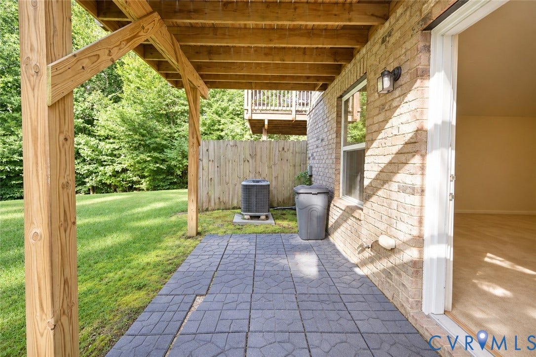 Brick exterior featuring a covered patio with patterned pavers, a sliding glass door, and a window