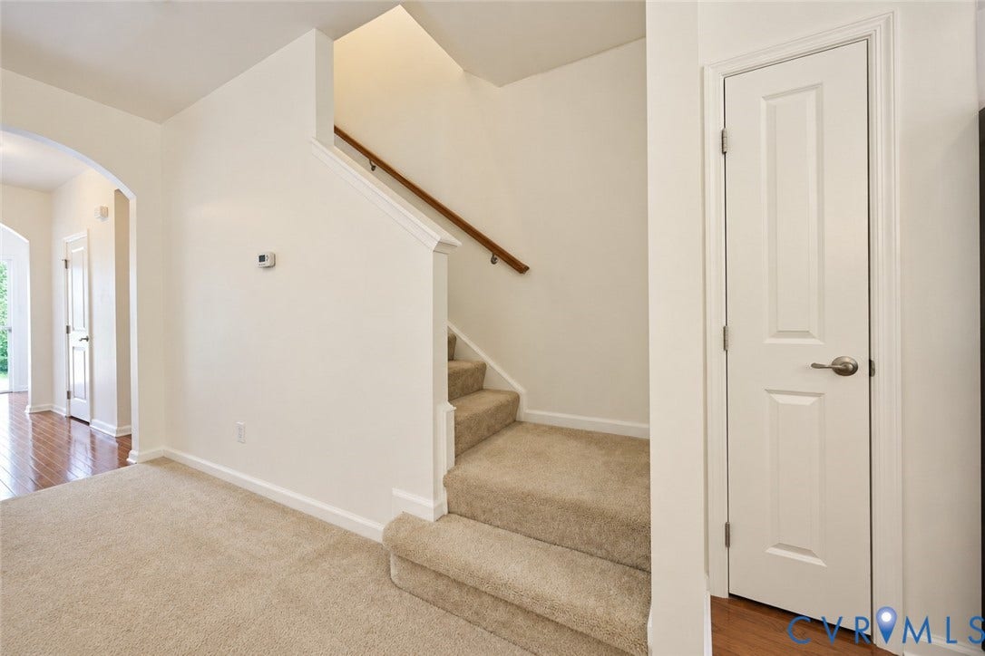 Carpeted staircase with wood handrail, arched doorway, and hardwood flooring