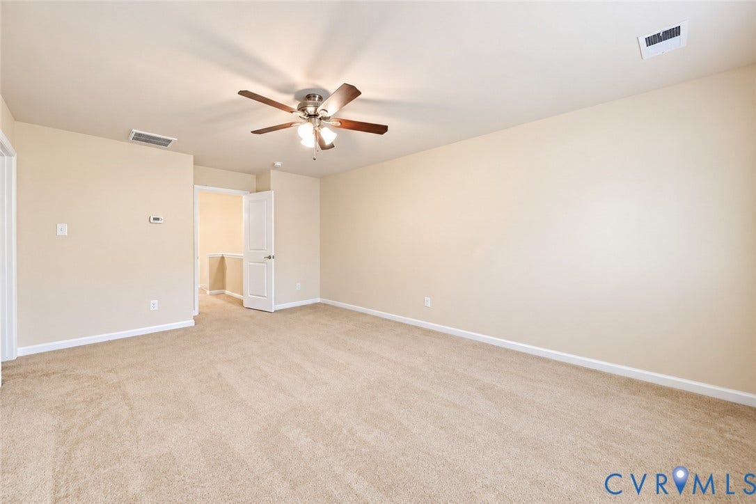 Neutral-toned carpeting, ceiling fan with light fixture, and a white interior door