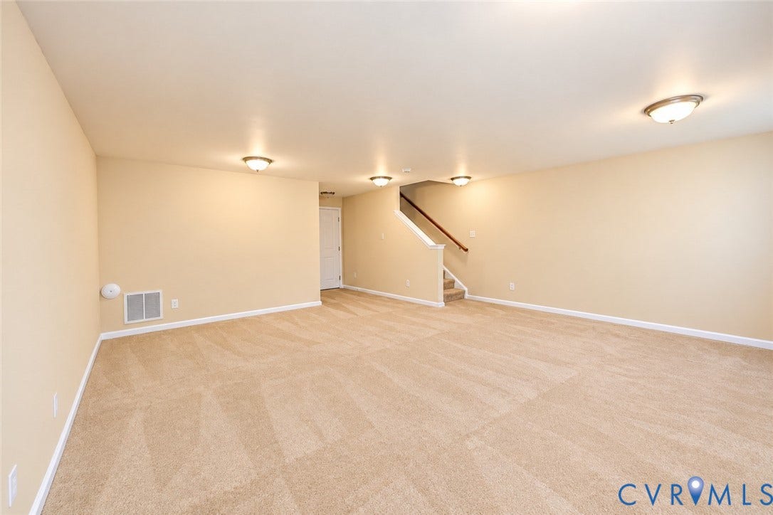 Spacious carpeted room with neutral wall tones and multiple flush-mount ceiling lights