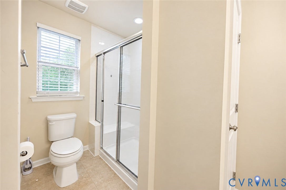 Bathroom featuring a glass-enclosed shower, white toilet, tiled flooring, and a window with blinds
