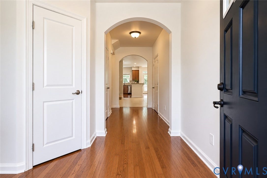 Hardwood flooring throughout the entry, arched doorways, white interior doors, and a dark paneled entry door