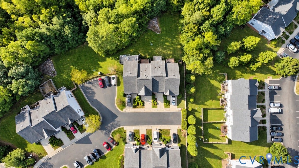 Community setting featuring multiple residential buildings with private driveways, designated parking areas, ample green space, and mature tree lines