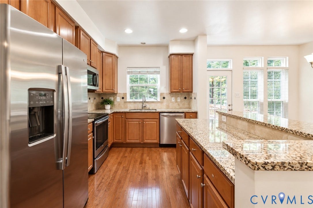 Kitchen featuring wood-finish flooring, stainless steel appliances, granite countertops, wood cabinetry, and a tile backsplash