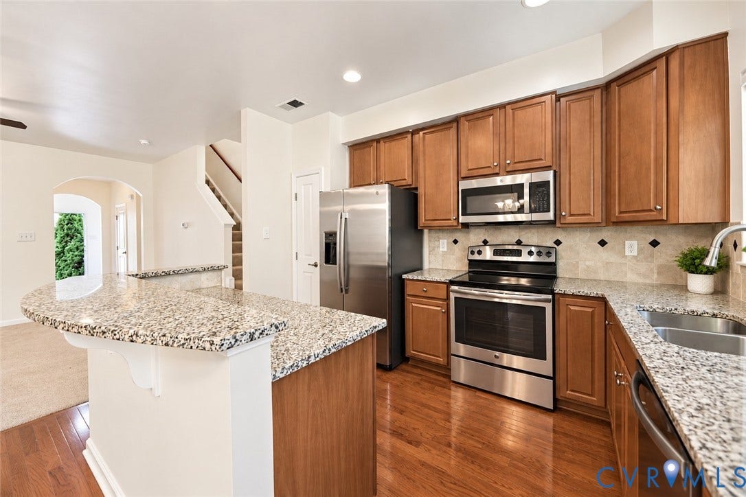 Kitchen featuring wood-finish flooring, stainless steel appliances, granite countertops, wood cabinetry, and a tile backsplash