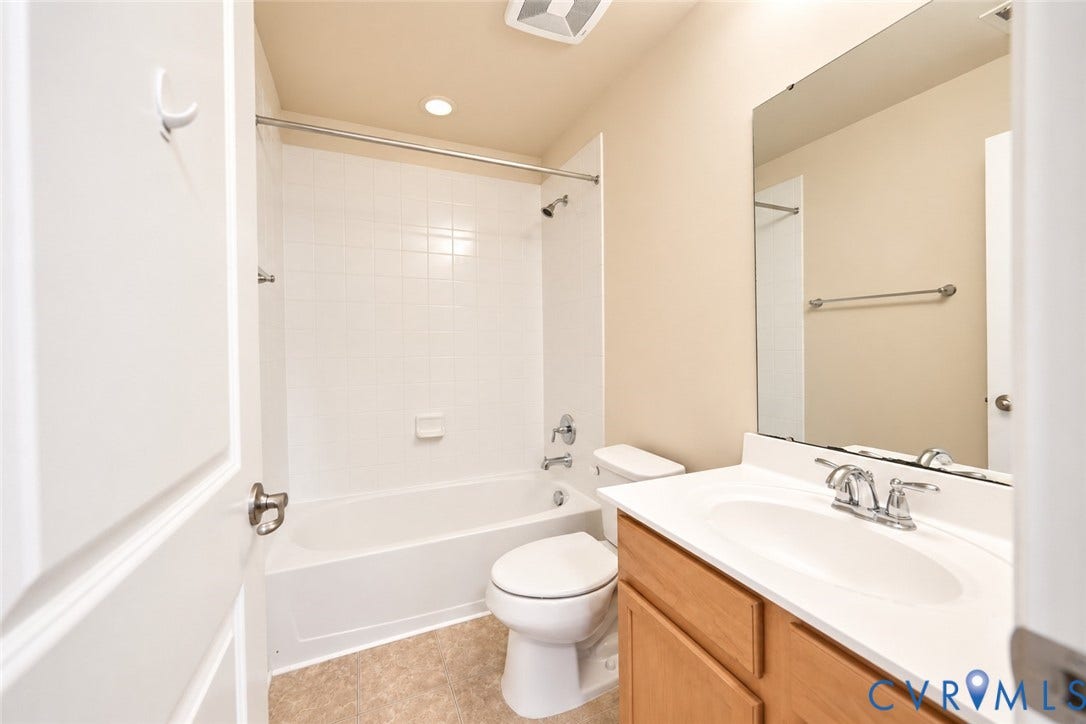 Bathroom featuring a tub/shower combination with white tile surround, a single vanity with wood-finish cabinetry, and a wall-mounted mirror