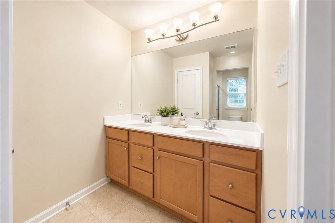 Double vanity with wood-finish cabinetry, dual undermount sinks, and a large wall-mounted mirror