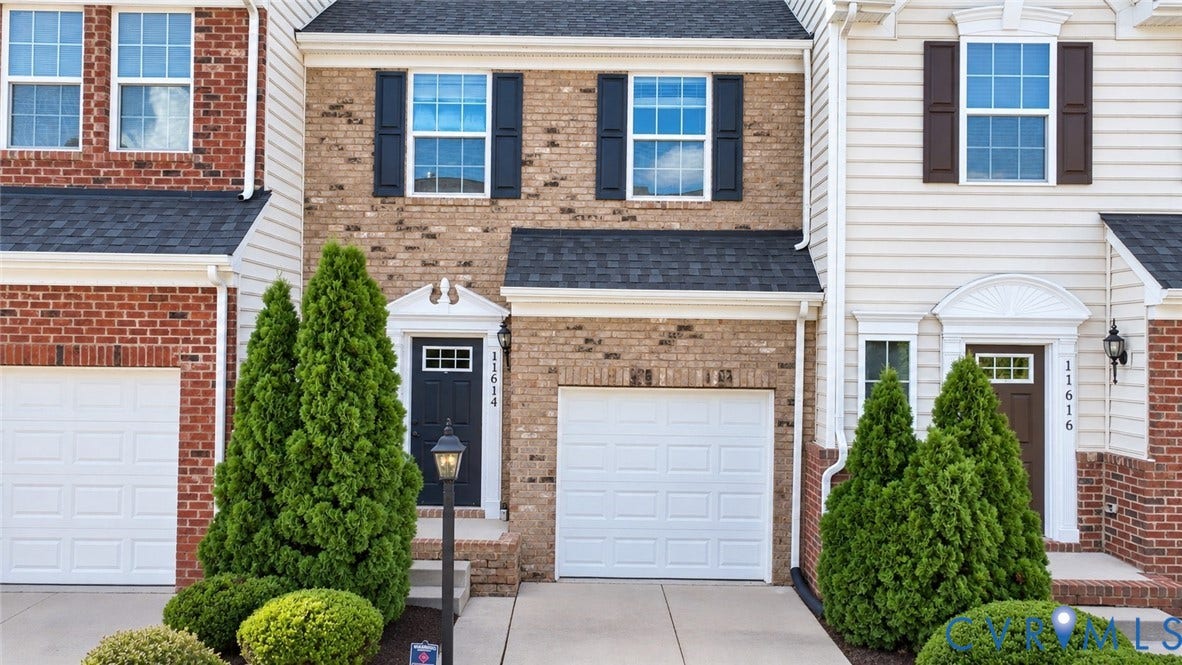Brick and siding exterior with a dark-paneled front door, white garage door, and a decorative portico