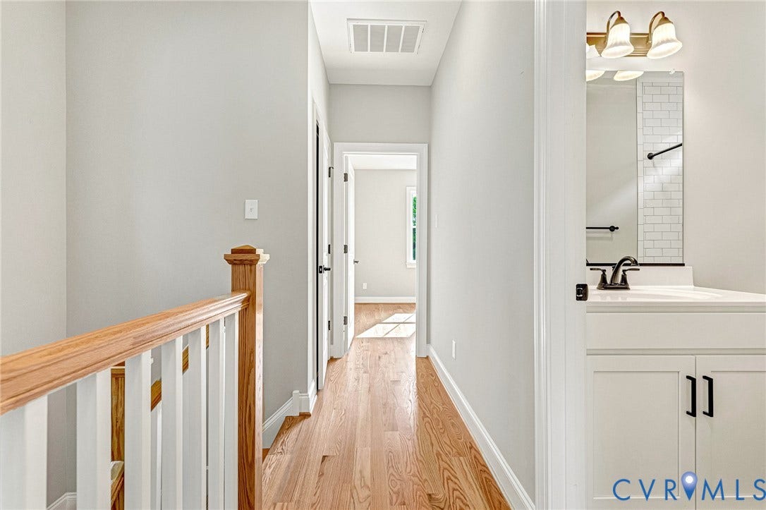 310 E 33rd Street, Swansboro West, Richmond, VA 23224 Hardwood flooring in the hallway, white painted walls, wood railing with white spindles, white vanity with a dark faucet, subway tile backsplash in the bathroom