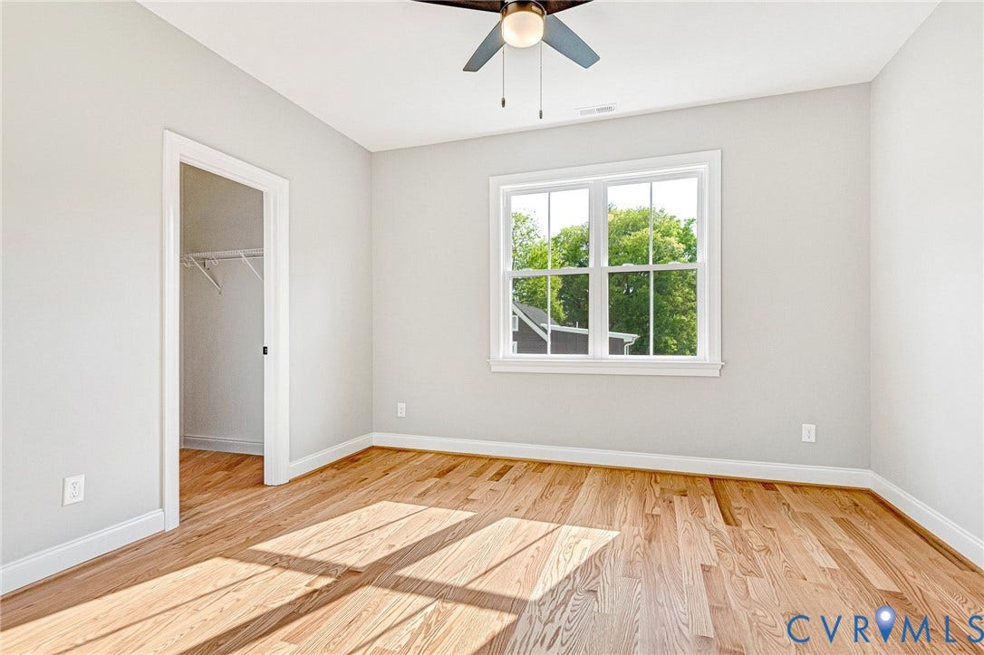 310 E 33rd Street, Swansboro West, Richmond, VA 23224 Bright, sunlit bedroom featuring hardwood flooring, large double-hung windows with natural light, ceiling fan with integrated lighting, and a walk-in closet with shelving and hanging rod