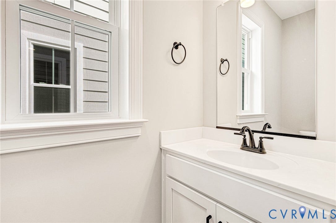 310 E 33rd Street, Swansboro West, Richmond, VA 23224 White vanity with an integrated sink and a dark bronze faucet, complemented by a large wall-mounted mirror and a window with white trim