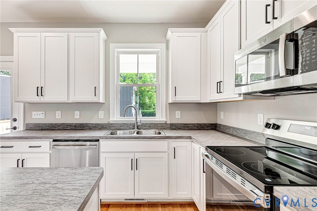 310 E 33rd Street, Swansboro West, Richmond, VA 23224 White shaker-style cabinetry with matte black hardware, stainless steel appliances, a double basin sink, light-toned countertop, and wood-finish flooring