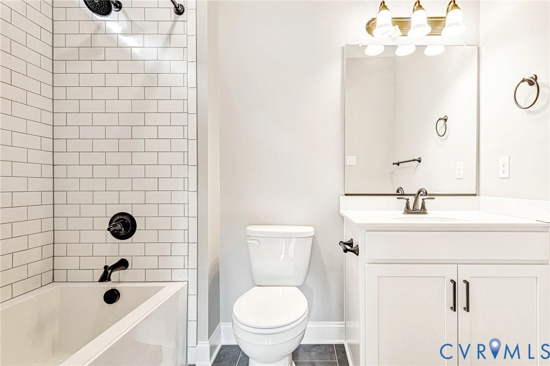 310 E 33rd Street, Swansboro West, Richmond, VA 23224 Bathtub with subway tile surround and matte black fixtures, white vanity with integrated sink, rectangular mirror, and dark tile flooring