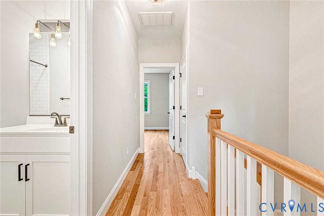 308 E 33rd Street, Swansboro West, Richmond, VA 23224 Hardwood flooring, white wall paint, white bathroom vanity with dark hardware, white subway tile shower surround, and a natural wood staircase handrail