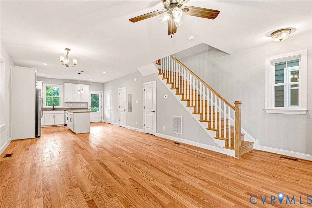 308 E 33rd Street, Swansboro West, Richmond, VA 23224 Hardwood flooring throughout, a staircase with wooden treads and white risers, a kitchen island with pendant lighting, white kitchen cabinetry, and an attached ceiling fan with lighting