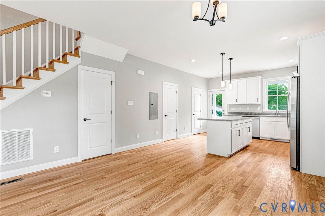 306 E 33rd Street, Swansboro West, Richmond, VA 23224 Hardwood flooring throughout, white shaker kitchen cabinetry, kitchen island with seating, stainless steel appliances, and a staircase with white balusters