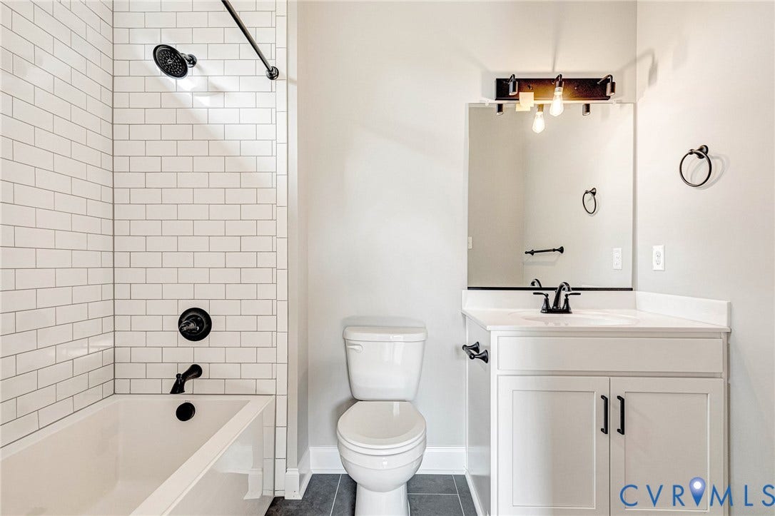 306 E 33rd Street, Swansboro West, Richmond, VA 23224 White subway tile shower surround with matte black fixtures, a white vanity with shaker-style cabinetry, and a countertop with an integrated sink
