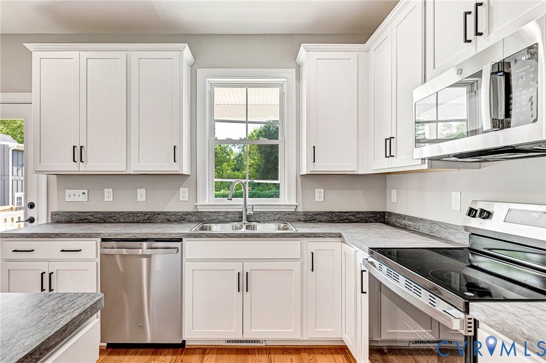 306 E 33rd Street, Swansboro West, Richmond, VA 23224 White shaker-style cabinetry with black hardware, stainless steel appliances, dark stone-finish countertops, and wood-finish flooring
