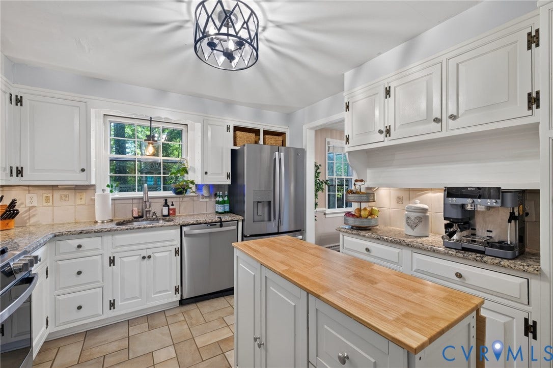 White cabinetry, stainless steel appliances, butcher block island, stone countertops, and tile flooring