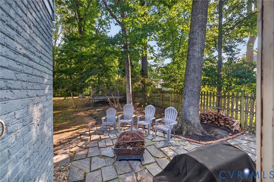 Stone patio with a fire pit, surrounded by mature trees and a wood fence