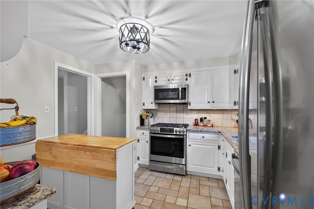 White cabinetry with black hardware, stainless steel appliances, light-toned tiled flooring, and a kitchen island with a wood-finish countertop