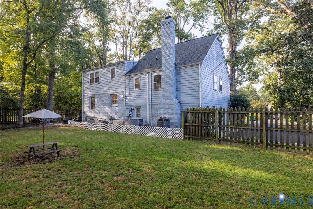 Expansive green lawn with a privacy fence, wood siding, and a brick chimney