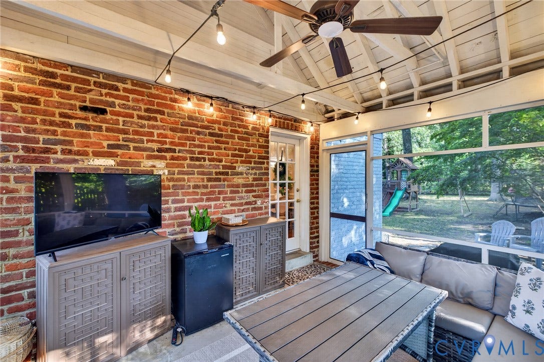 Screened porch with exposed brick wall, white wood-beamed ceiling, and a ceiling fan