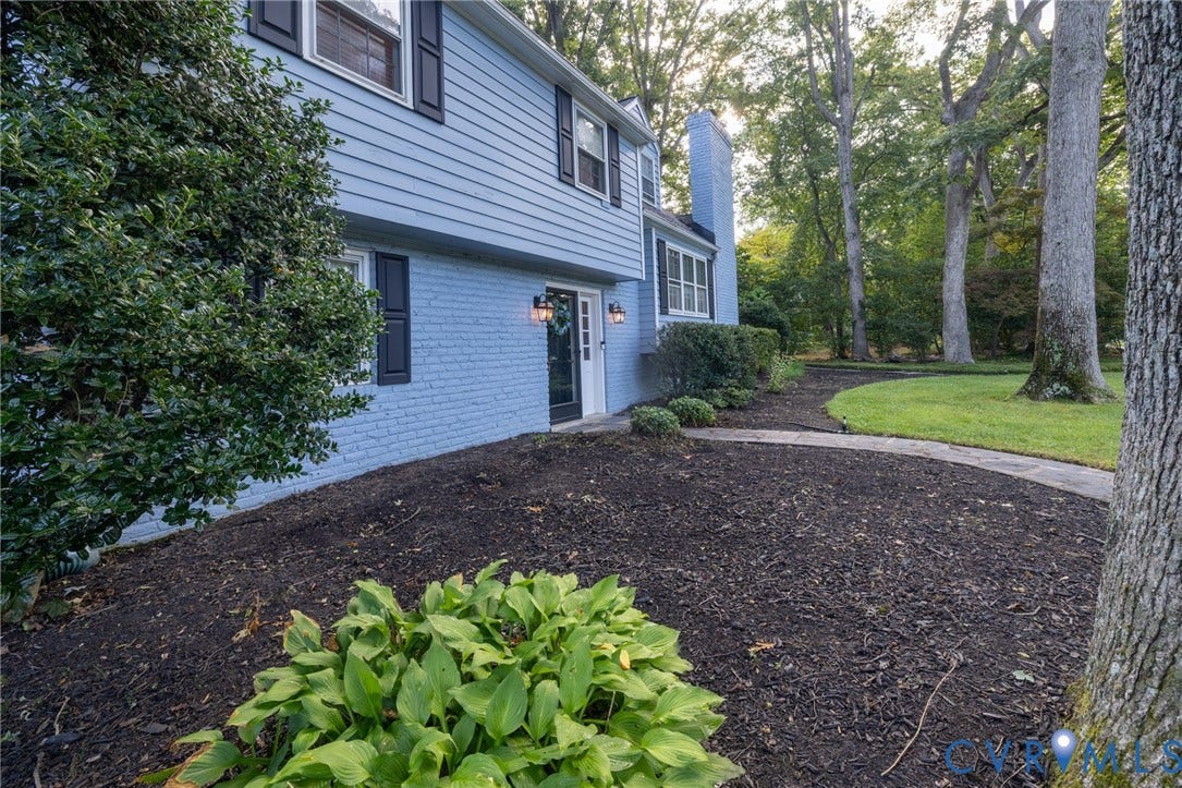 Two-story exterior with light blue siding and brick, black window shutters, a front entry door with exterior lighting, and a curved concrete walkway
