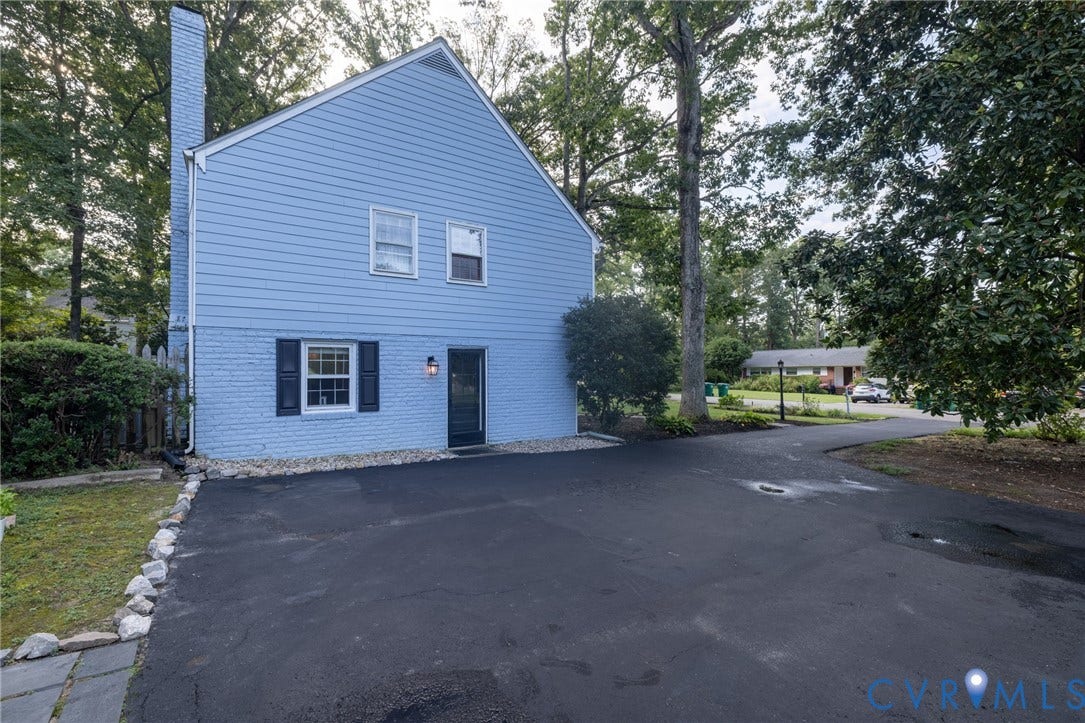 Two-story residence featuring light blue siding, a prominent brick chimney, and a black shingle roof