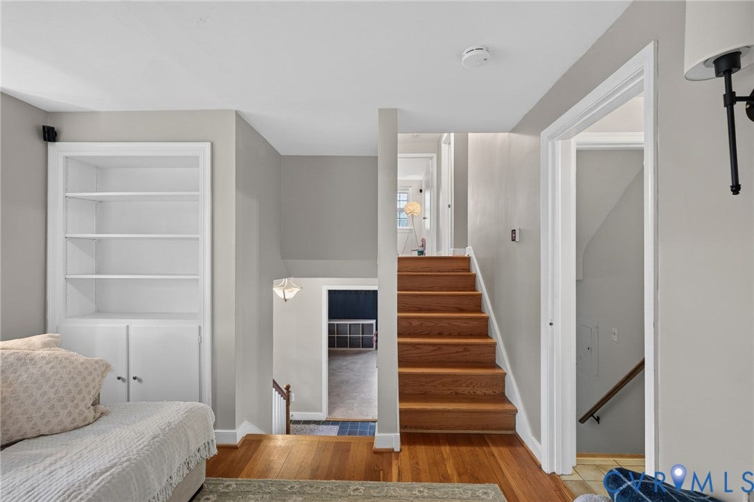 Hardwood flooring, built-in shelving with cabinetry, wood staircase, and interior wall sconce