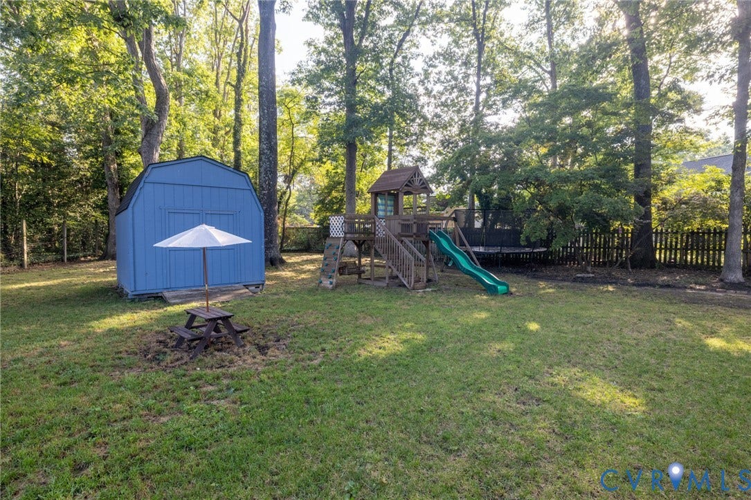 Expansive backyard featuring a blue storage shed, a playset with a green slide, and mature trees
