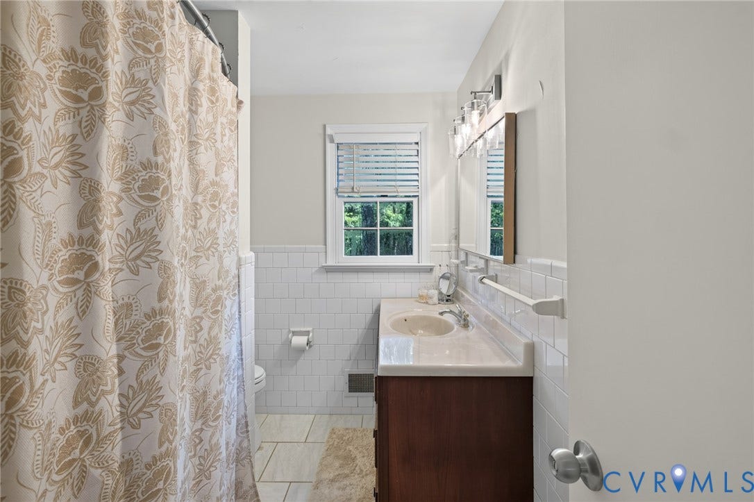 Bathroom featuring a wood-finish vanity with an integrated sink, white subway tile wainscoting, a window with blinds, and tile flooring