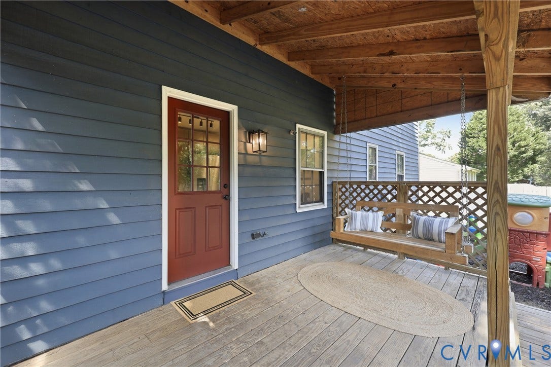 9349 Shiloh Drive, Chesterfield, VA 23237 Covered porch with wood-finish decking, blue siding, a red entry door with glass panels, and an exterior wall light fixture