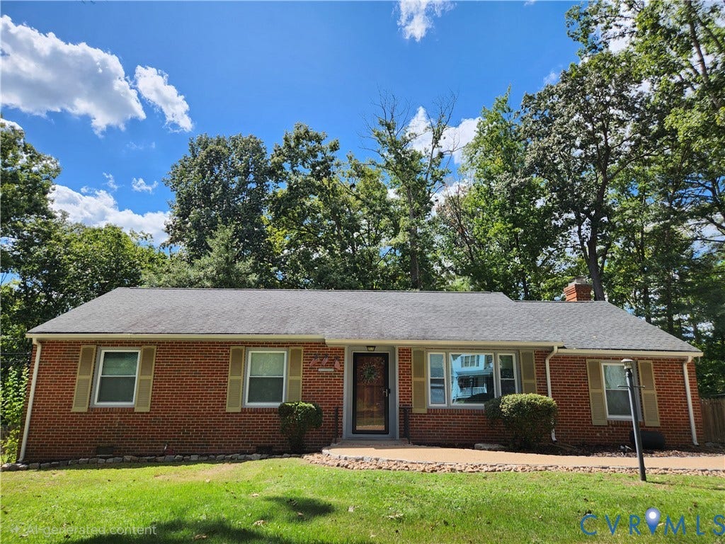 Brick exterior with a shingled roof, mature trees, a paved walkway, and a prominent front door