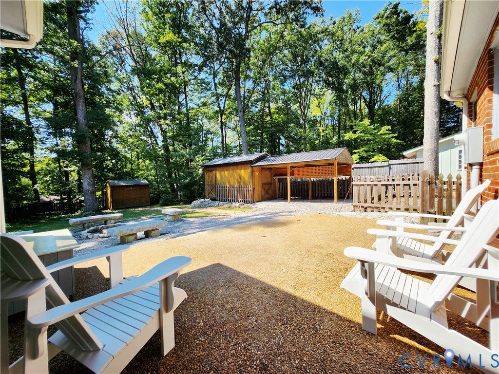 Expansive gravel patio featuring a built-in fire pit with stone benches, a covered outdoor structure, and a secondary storage shed