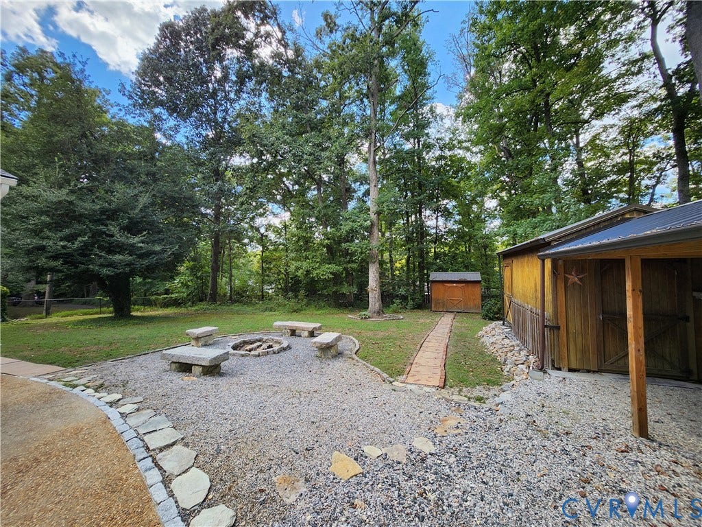Gravel patio featuring a built-in fire pit with stone benches, a wooden storage shed, and a wooden accessory structure with a covered porch