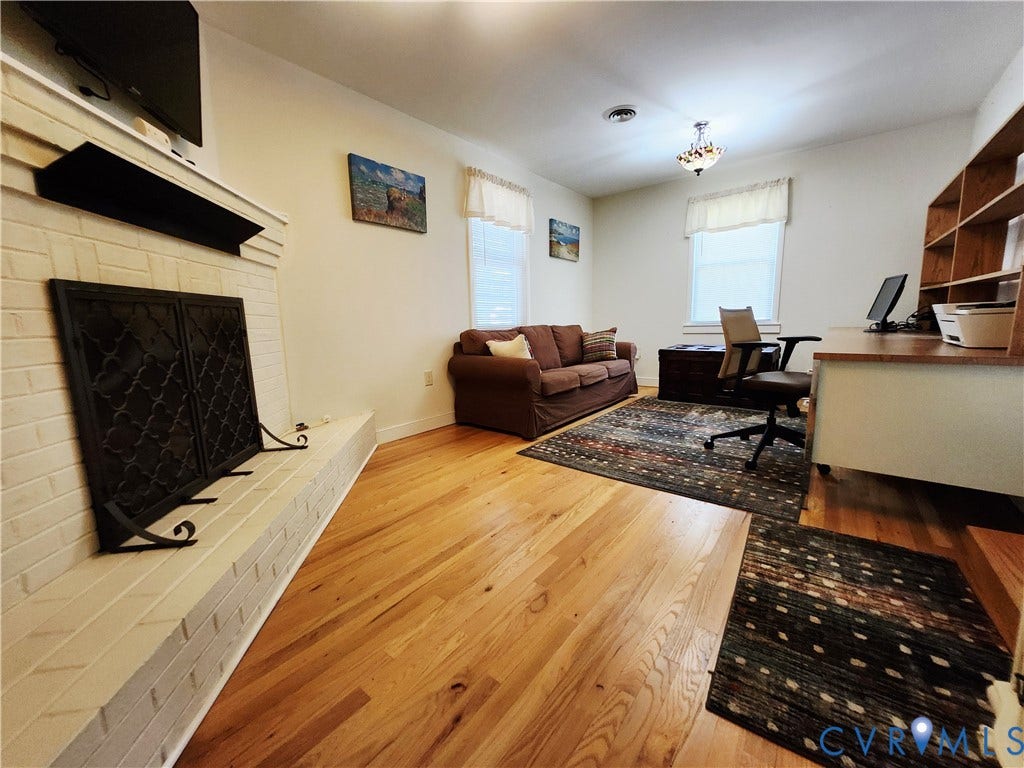 Hardwood flooring, white brick fireplace with hearth, white walls, built-in shelving, and multiple windows