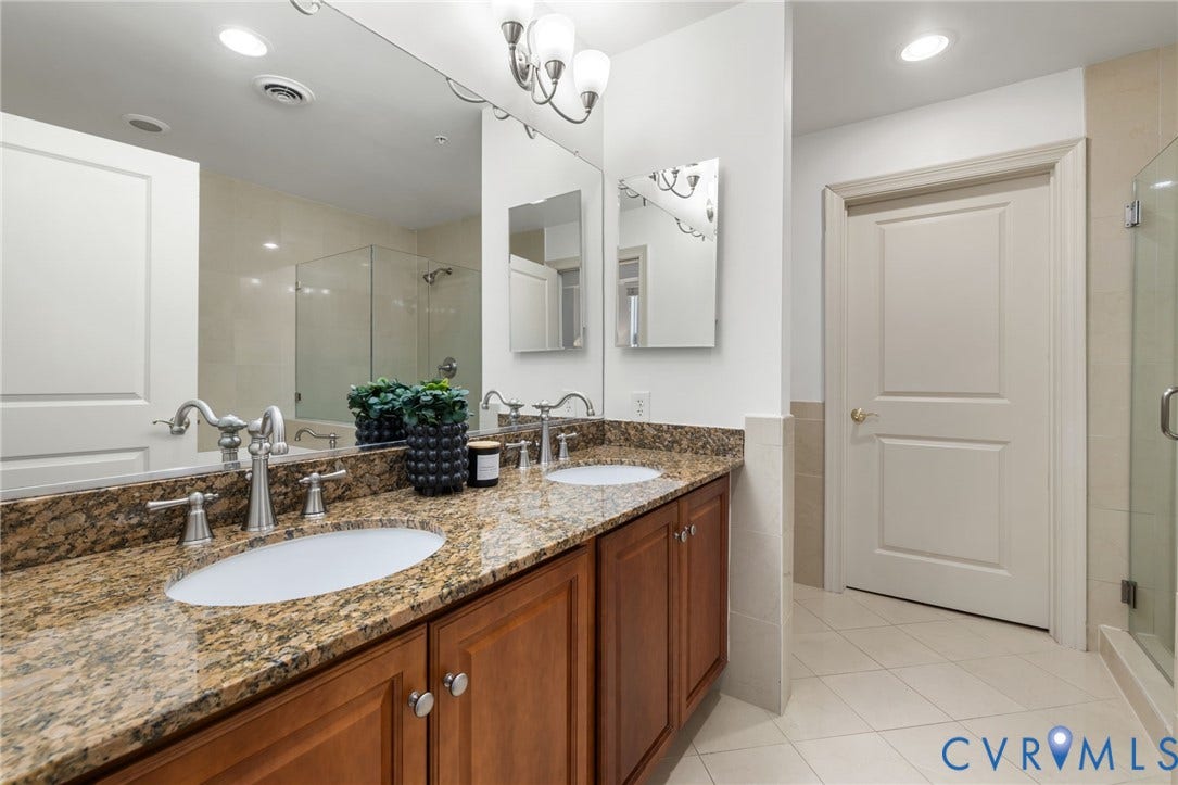 6 N 6th Street, #U5B, Downtown/Financial District, Richmond, VA 23219 Dual vanity with stone countertop and integrated sinks, brushed nickel fixtures, wood-finish cabinetry, and a glass-enclosed shower