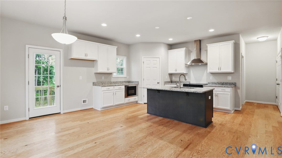 Kitchen with wood-finish flooring, white cabinetry, a central island with a sink, and stainless steel appliances