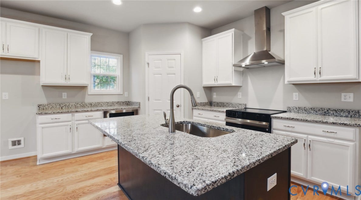 Kitchen featuring an expansive central island with an integrated sink, granite countertops, white cabinetry, a stainless steel range hood, and wood-finish flooring